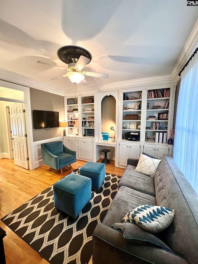 living room with built in shelves, light wood-type flooring, ceiling fan, and crown molding