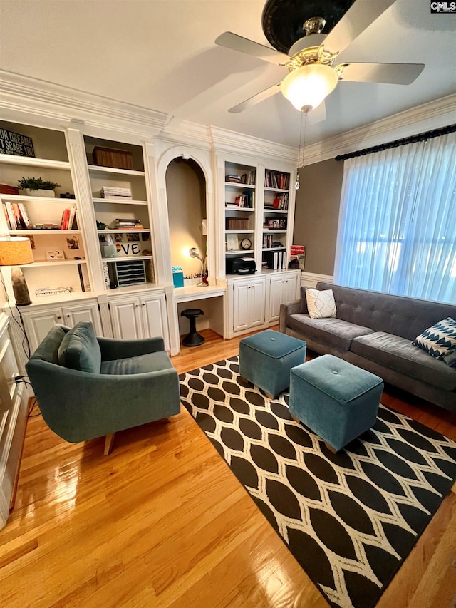 living room with built in shelves, crown molding, ceiling fan, and light wood-type flooring