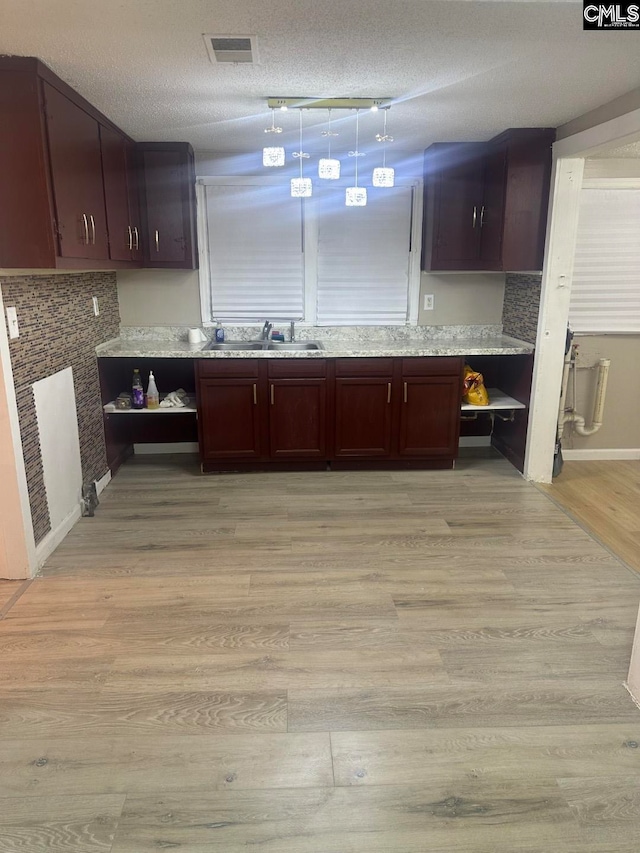 kitchen with sink, light stone countertops, a textured ceiling, dark brown cabinets, and light hardwood / wood-style floors