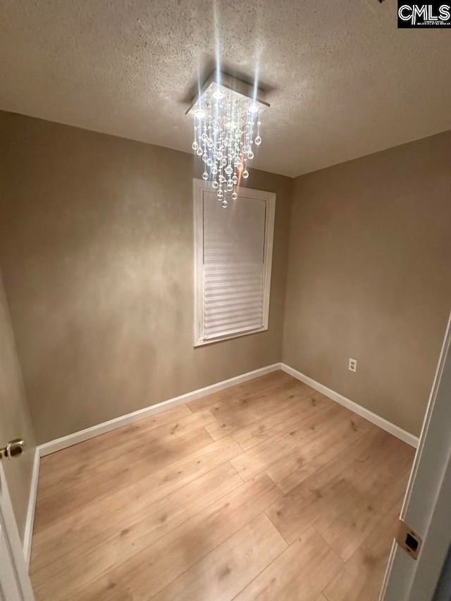 spare room featuring a chandelier, a textured ceiling, and hardwood / wood-style flooring