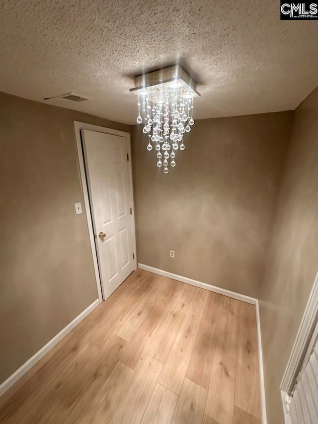 unfurnished dining area with a textured ceiling, hardwood / wood-style flooring, and an inviting chandelier