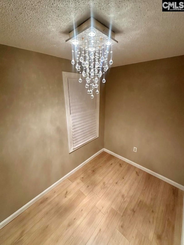 unfurnished dining area featuring vaulted ceiling, a chandelier, a textured ceiling, and hardwood / wood-style flooring