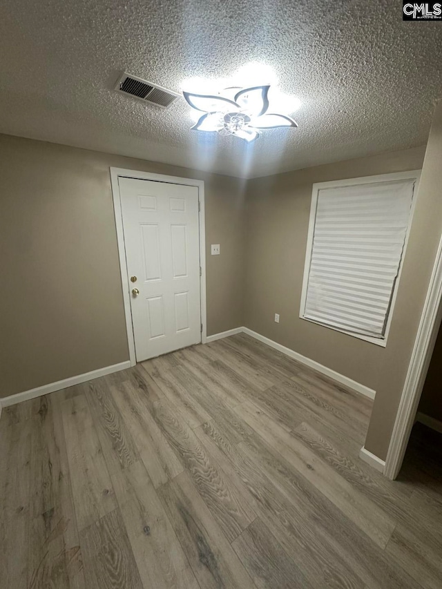 spare room with a textured ceiling and light hardwood / wood-style floors