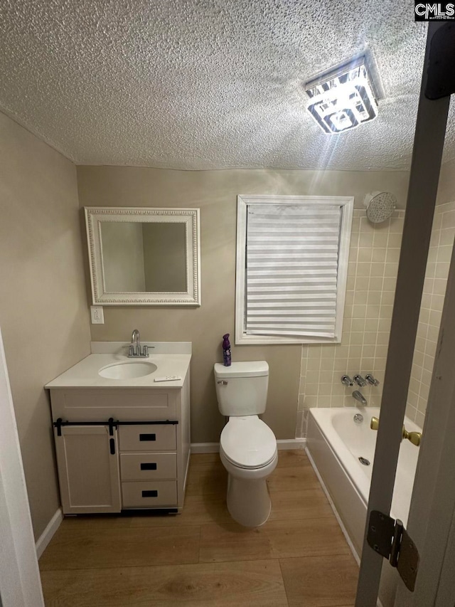 bathroom with a tub to relax in, a textured ceiling, toilet, vanity, and hardwood / wood-style flooring