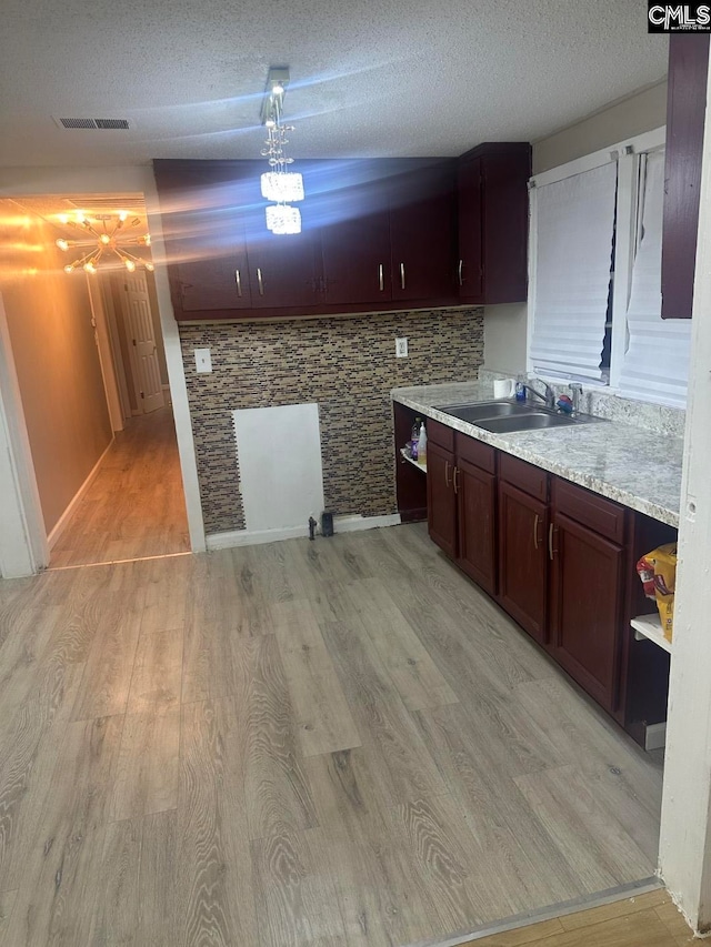 kitchen featuring a textured ceiling, sink, hanging light fixtures, and light hardwood / wood-style flooring