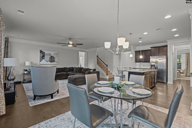 dining space featuring crown molding, sink, dark wood-type flooring, and ceiling fan with notable chandelier