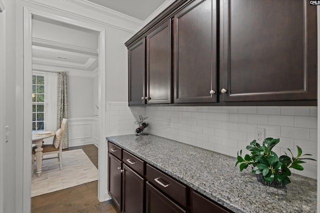 kitchen featuring crown molding, dark hardwood / wood-style floors, tasteful backsplash, light stone counters, and dark brown cabinetry