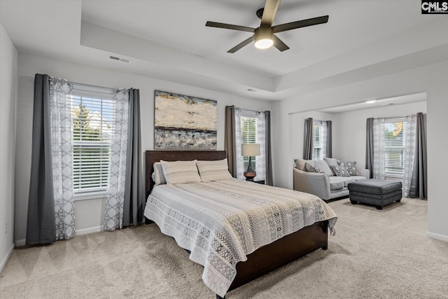 bedroom featuring multiple windows, carpet floors, a raised ceiling, and ceiling fan