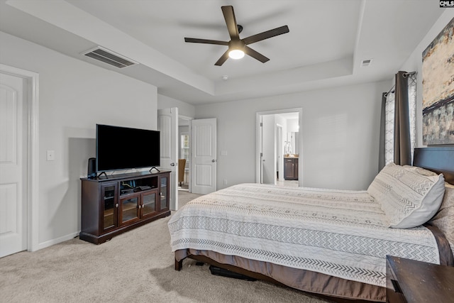 bedroom with a tray ceiling, connected bathroom, ceiling fan, and light carpet