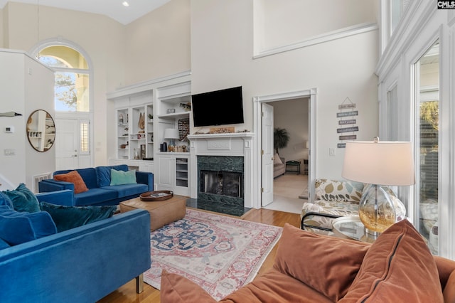 living room featuring a high end fireplace, a towering ceiling, light hardwood / wood-style flooring, and built in shelves