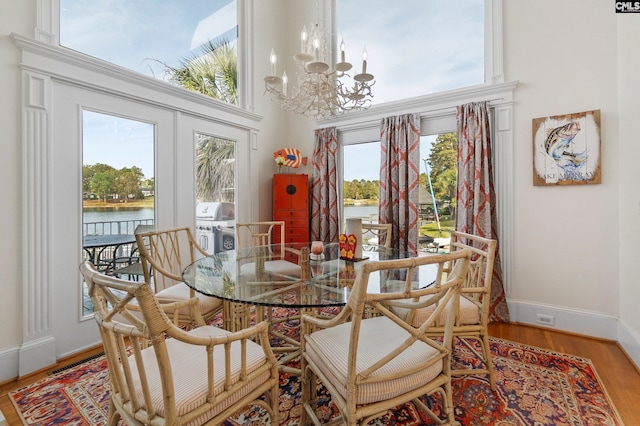 dining area with an inviting chandelier, light hardwood / wood-style floors, a water view, and a high ceiling