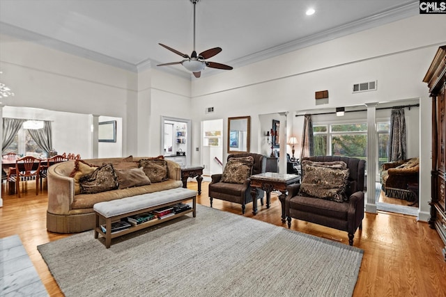 living room with a high ceiling, crown molding, light hardwood / wood-style flooring, ceiling fan, and decorative columns