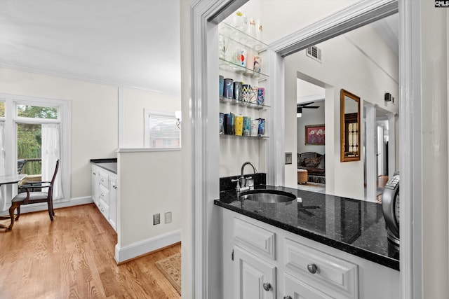 bar featuring sink, white cabinets, dark stone counters, and light wood-type flooring