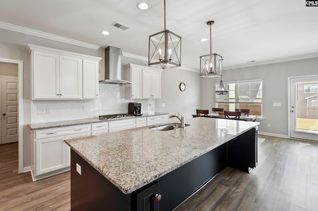 kitchen with wall chimney exhaust hood, dark wood-type flooring, decorative light fixtures, a center island with sink, and white cabinets