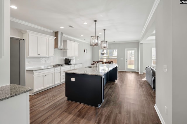 kitchen featuring stainless steel appliances, white cabinetry, wall chimney exhaust hood, and a center island with sink