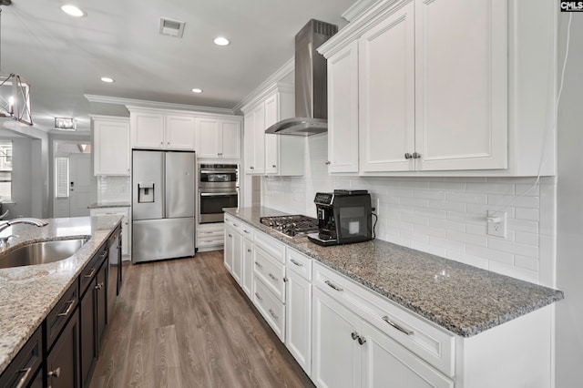 kitchen with white cabinetry, sink, wall chimney range hood, hardwood / wood-style floors, and appliances with stainless steel finishes