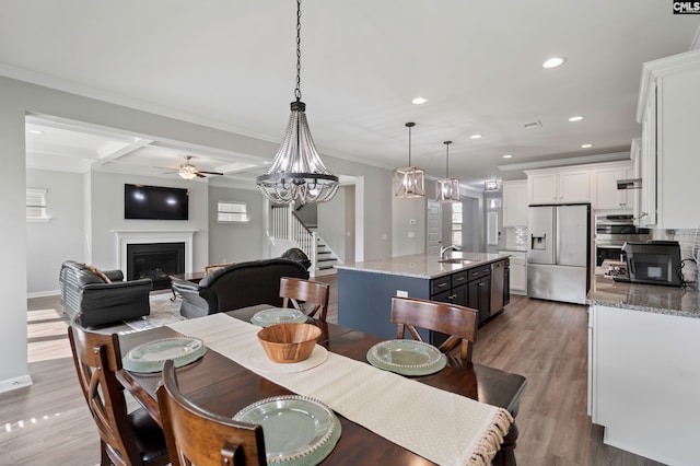 dining room featuring ceiling fan with notable chandelier, crown molding, sink, light wood-type flooring, and beam ceiling