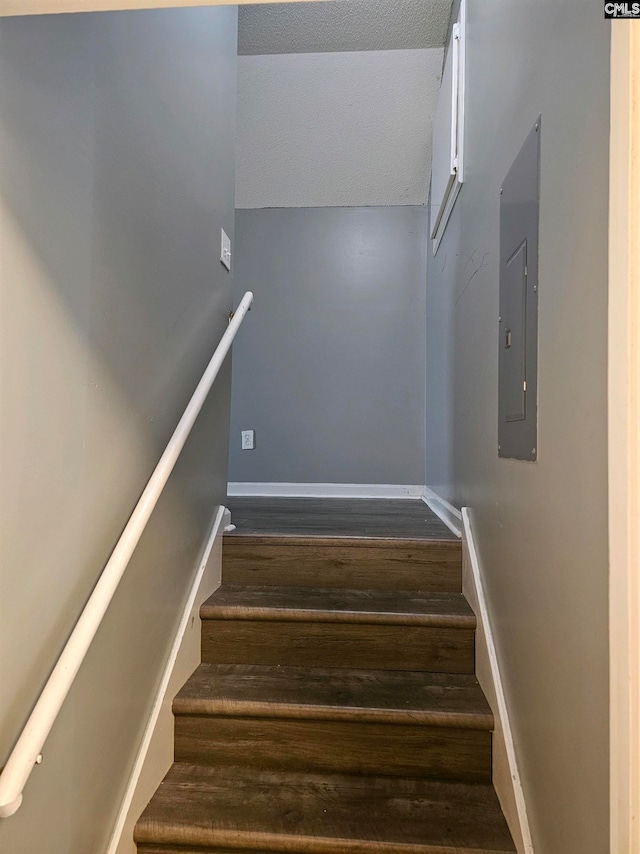 stairs with electric panel, wood-type flooring, and a textured ceiling