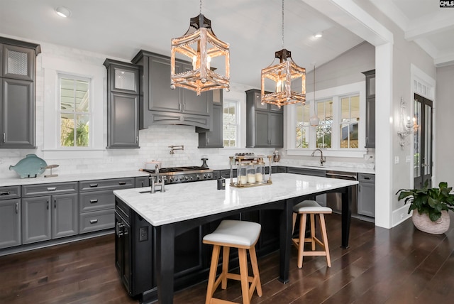 kitchen featuring tasteful backsplash, sink, decorative light fixtures, dark hardwood / wood-style floors, and an island with sink