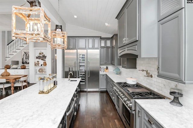 kitchen with gray cabinetry, dark wood-type flooring, decorative light fixtures, lofted ceiling, and high quality appliances