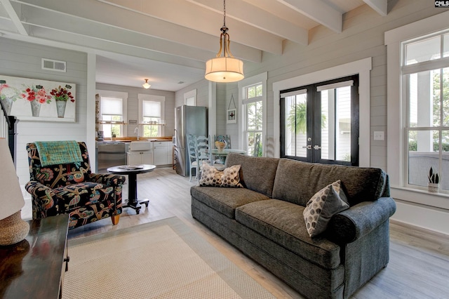 living room with wooden walls, light wood-type flooring, a wealth of natural light, and french doors