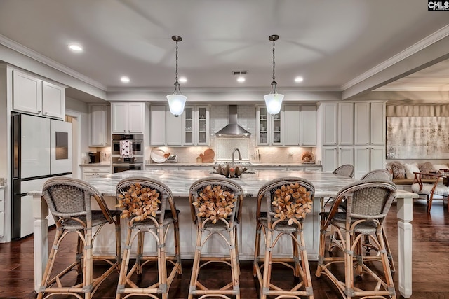 kitchen featuring wall chimney exhaust hood, dark hardwood / wood-style floors, refrigerator, decorative light fixtures, and a kitchen island with sink