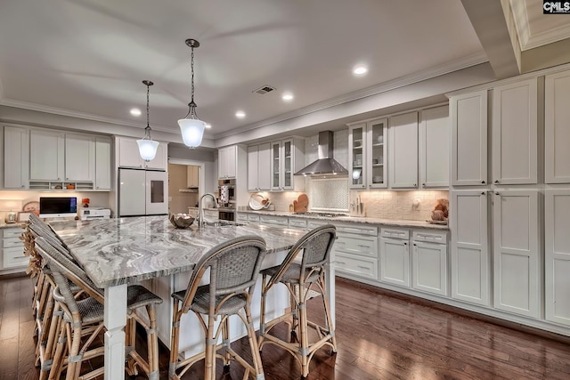 kitchen with dark wood-type flooring, white refrigerator, wall chimney range hood, decorative light fixtures, and a large island