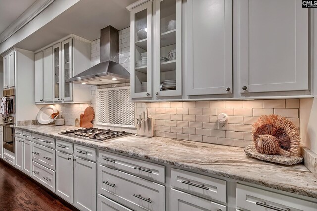 kitchen featuring backsplash, dark wood-type flooring, white cabinets, wall chimney exhaust hood, and stainless steel gas cooktop