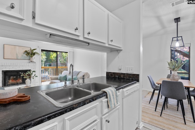 kitchen with a brick fireplace, white dishwasher, sink, pendant lighting, and white cabinets