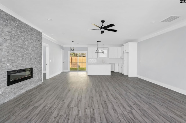 unfurnished living room featuring dark hardwood / wood-style floors, ceiling fan, ornamental molding, and a fireplace