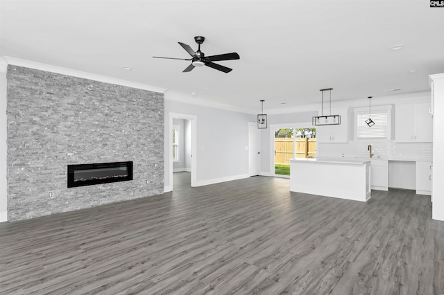 unfurnished living room featuring crown molding, a stone fireplace, dark hardwood / wood-style floors, and ceiling fan