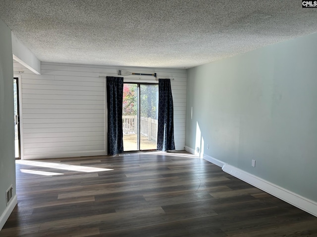 empty room featuring wooden walls, dark hardwood / wood-style flooring, and a textured ceiling