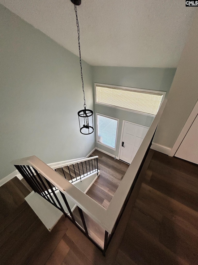 stairs featuring a textured ceiling, hardwood / wood-style flooring, vaulted ceiling, and a notable chandelier