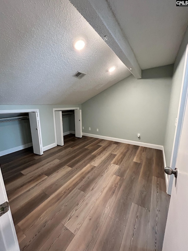 unfurnished bedroom with beam ceiling, a textured ceiling, and dark hardwood / wood-style floors