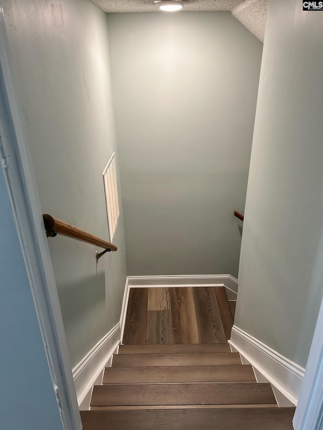 stairs featuring a textured ceiling and hardwood / wood-style flooring