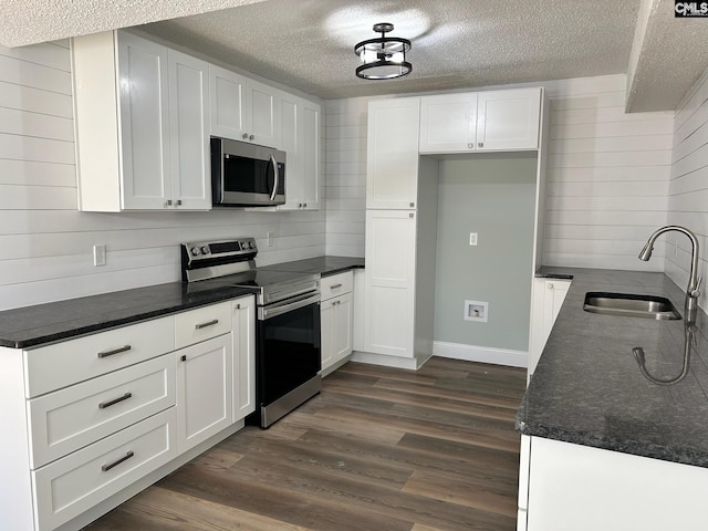 kitchen with appliances with stainless steel finishes, dark hardwood / wood-style floors, white cabinetry, and sink