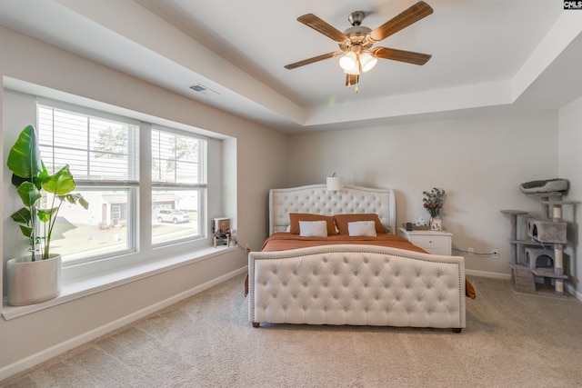 bedroom with light colored carpet, ceiling fan, and a tray ceiling