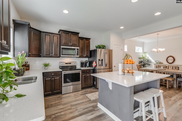 kitchen with a kitchen island, an inviting chandelier, appliances with stainless steel finishes, and light hardwood / wood-style flooring