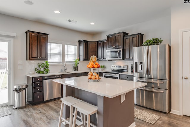 kitchen featuring appliances with stainless steel finishes, tasteful backsplash, dark brown cabinetry, light hardwood / wood-style flooring, and a kitchen island