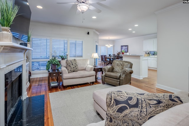 living room with crown molding, ceiling fan with notable chandelier, and light wood-type flooring