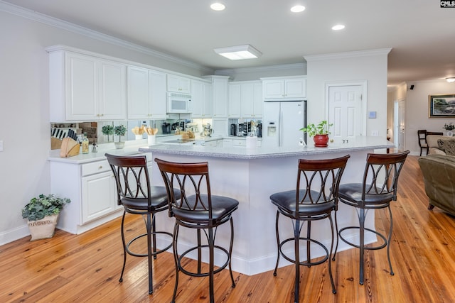 kitchen with a breakfast bar area, white cabinets, ornamental molding, white appliances, and light hardwood / wood-style flooring