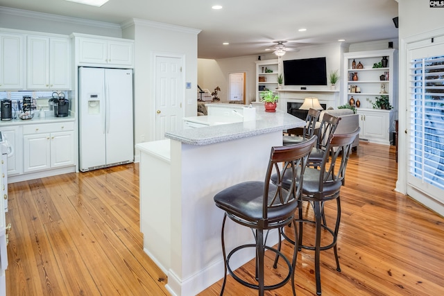 kitchen featuring white cabinetry, a breakfast bar area, white refrigerator with ice dispenser, ceiling fan, and crown molding