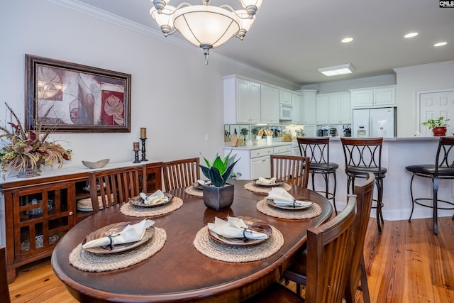 dining area with an inviting chandelier, ornamental molding, and light hardwood / wood-style flooring