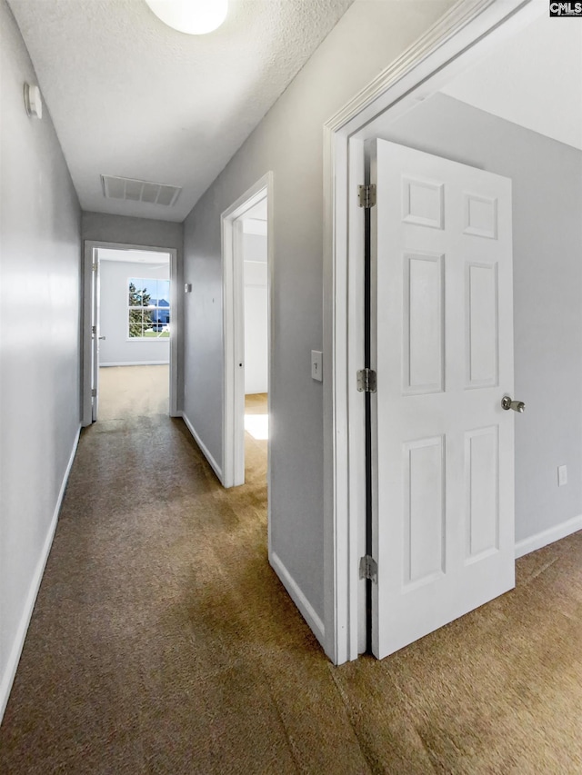 hall featuring carpet flooring and a textured ceiling