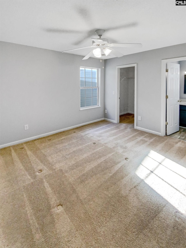 unfurnished bedroom with ceiling fan, a spacious closet, ensuite bathroom, light colored carpet, and a closet