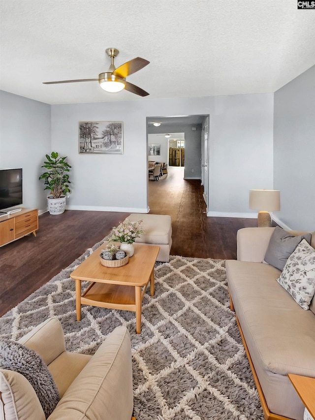 living room with a textured ceiling, ceiling fan, and dark wood-type flooring