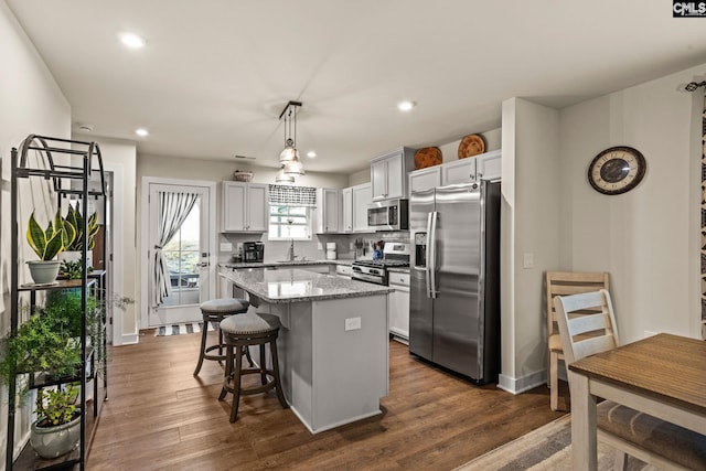 kitchen with light stone countertops, a center island, stainless steel appliances, dark hardwood / wood-style floors, and decorative light fixtures