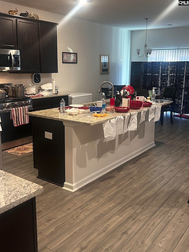 kitchen with a kitchen island with sink, hanging light fixtures, dark hardwood / wood-style floors, a notable chandelier, and stainless steel appliances