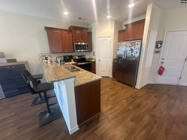 kitchen with light stone countertops, dark hardwood / wood-style flooring, kitchen peninsula, a breakfast bar area, and appliances with stainless steel finishes