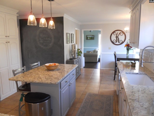 kitchen with light stone countertops, sink, gray cabinets, a kitchen island, and ornamental molding